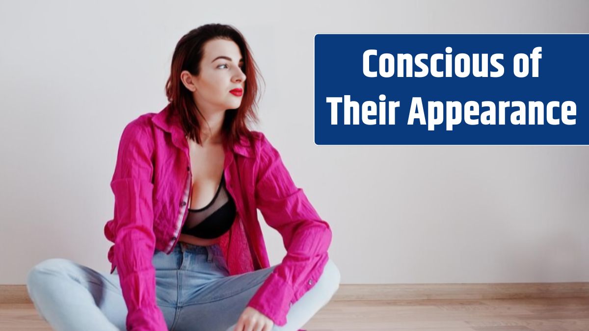 Red haired girl with a big bust on black bra and rose shirt against white wall at empty room.